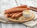 Raw frankfurter sausages with mustard on cutting board.