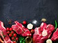 Raw fresh meat steak with cherry tomatoes, hot pepper, garlic, oil and herbs on dark stone, concrete background. Free space for your text