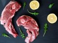 A lamb shoulder chops. Raw meat with lemon and asparagus on black stone.