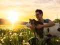 Farmer embracing calf on grass field during sunset