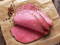 Peppered roast beef pastrami slices on paper with grains of coloured pepper